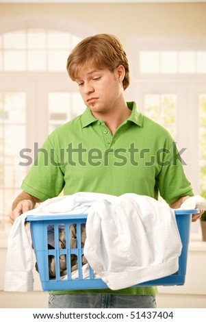 Young guy bored of housework holding a basket of clothes to do washing.