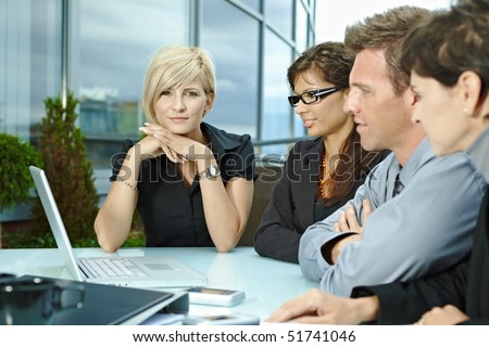 Group of young business people sitting in a row at table on office terrace outdoor, talking and working on laptop computer.