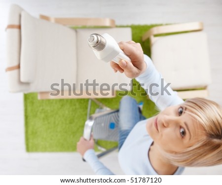 Woman in high angle view trying to change light bulb standing on ladder in living room looking up.Focus placed on light bulb.