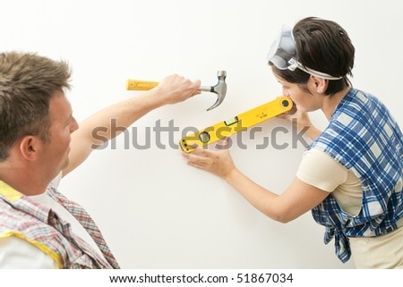 Couple working together on home renovation, woman holding spirit level tool, man holding hammer.
