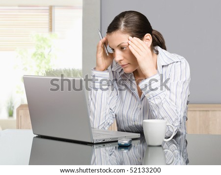 Young woman sitting at desk working with laptop computer at home, serious, thinking.