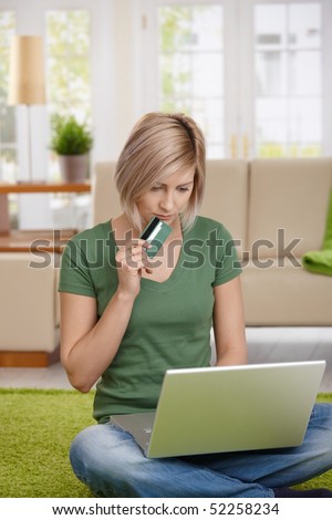 Young woman sitting on floor at home shopping online with credit card and laptop.