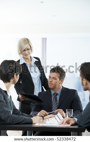 Assistant handing report to executive at meeting in office.
