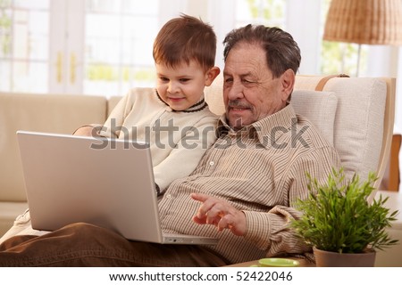 Grandfather together with grandson at home using laptop computer looking at screen.