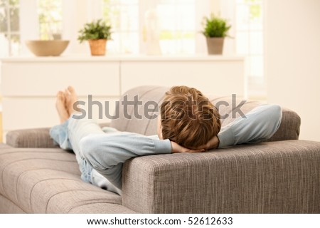 Man lying on back on sofa in  bright living room.