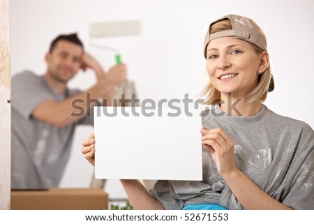 Smiling couple painting new house, woman in focus holding blank page, copyspace.