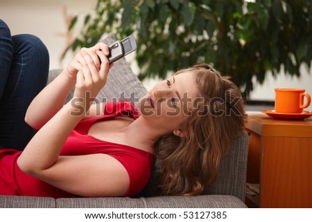 Happy teen girl looking at phone lying on couch at home.