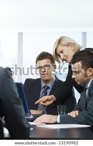 Business people looking at laptop, talking at meeting table in office,