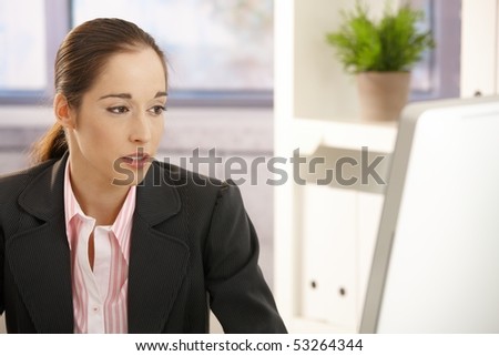 Young businesswoman sitting in office looking at screen.