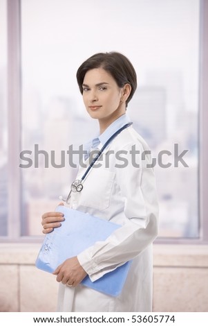 Portrait of attractive female doctor walking on hospital corridor, smiling at camera.