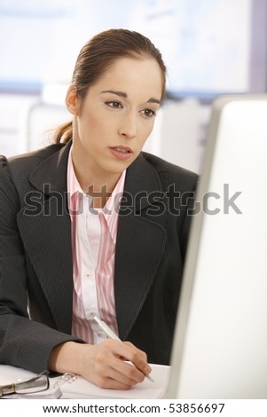 Tired businesswoman sitting at desk, working with computer, looking at screen.