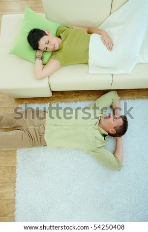 Couple sleeping at home on sofa and on floor. Overhead view.