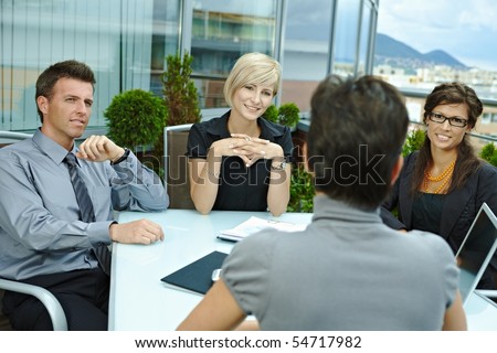 Group of young business people sitting around table on office terrace outdoor, talking and working together.