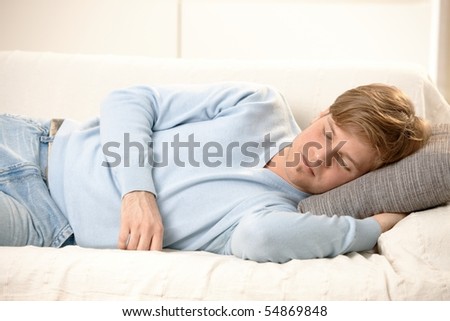 Tired young man sleeping on couch, taking afternoon nap.