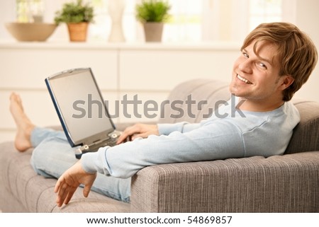 stock-photo-man-sitting-with-laptop-computer-on-sofa-with-feet-up-in-living-room-looking-back-at-camera-54869857.jpg
