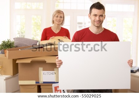 Smiling couple surrounded with boxes in new house, copyspace on blank poster.