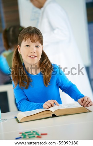 Elementary age schoolgirl looking at book in science class in primary school classroom.?