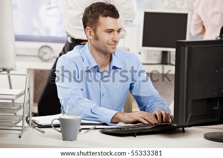 Casual businessman working in office, sitting at desk, typing on keyboard, looking at computer screen.?