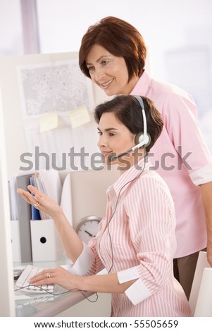 Customer care operator working at desk with supervisor, smiling.