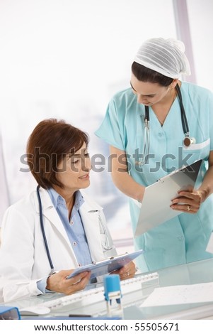Nurse and senior doctor analysing diagnosis together at office desk.