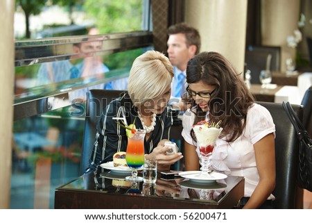 Young women sitting in cafe having sweets, looking at mobile phone.