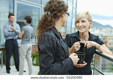 Businesswomen having break on office terrace outdoor drinking coffee talking.