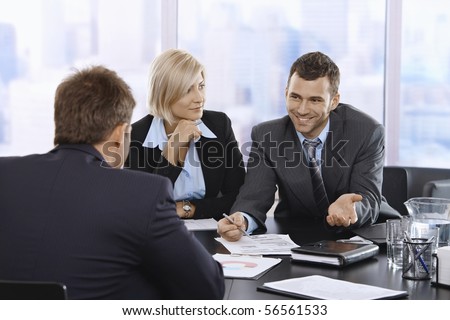 Smiling businessman discussing document at meeting with coworkers.