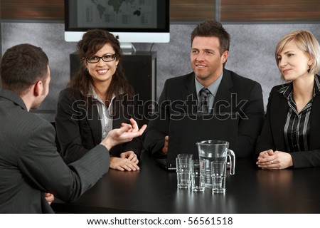 Young applicant explaining to panel of happy businesspeople during job interview in office.