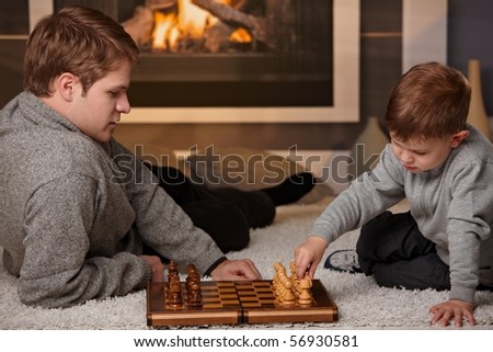 Father and 4 years old kid playing chess at home in a cold winter day.