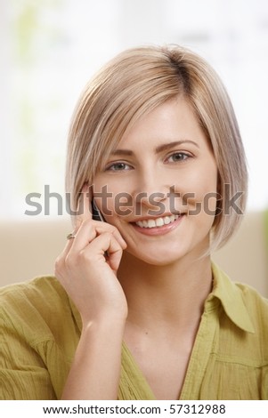 Portrait of attractive young woman speaking on mobile phone at home, smiling at camera. Copyspace on left.?