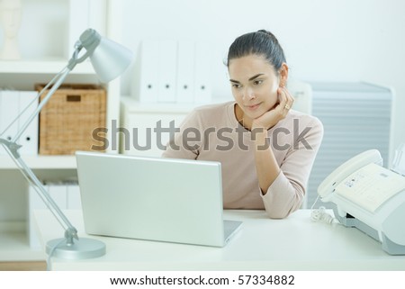 Attractive young woman sitting at desk, looking at laptop computer screen, thinking.