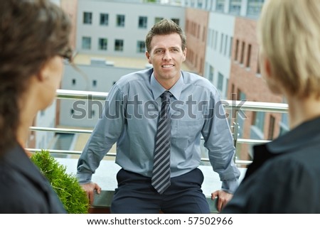 Business people talking on terrace of office building. Businessman in front, over the shoulder view.