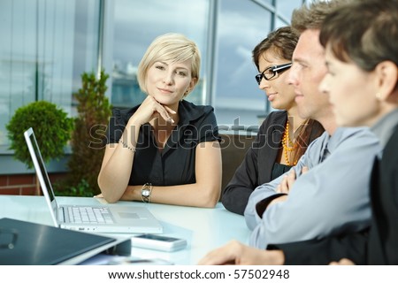 Group of young business people sitting in a row at table on office terrace outdoor, talking and working on laptop computer.