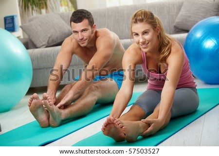 Young couple sitting on fitness mattress and streching legs before treining