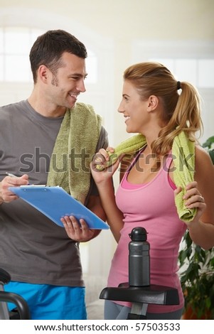 Young woman checking training plan with her personal trainer standing beside exercise bike at home.