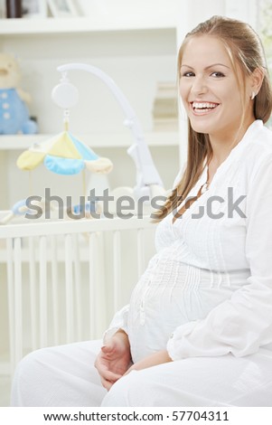 Portrait of happy pregnant woman sitting besides new crib, laughing.