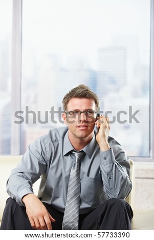 Elegant professional listening to call on cell phone sitting on beige leather sofa in sunlit room.?