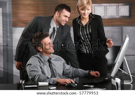 Businessman sitting at office desk, looking at screen together with colleagues, smiling.?