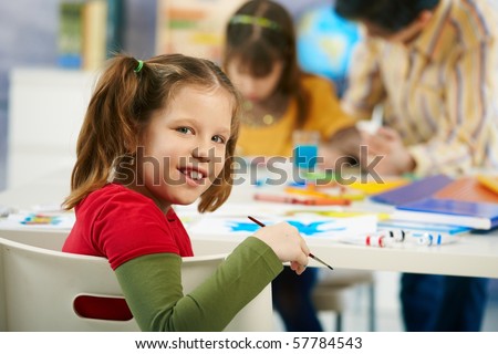 Portrait of happy elementary age child sitting at desk looking at camera in art class in primary school classroom, smiling.?