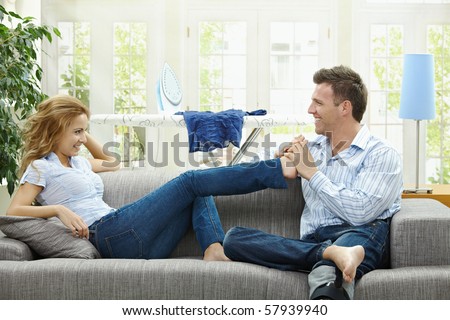 Couple relaxing at home on sofa, man giving foot massage to her gildfriend.