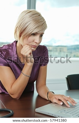 Young serious businesswoman sitting at table in office meeting room, working with laptop computer, thinking.