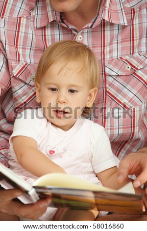 Cute baby girl (1-2 years toddler age) looking at book handheld by father.?