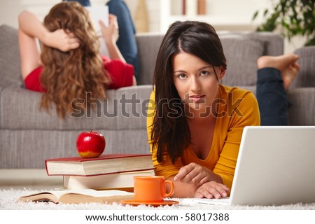 Teen girls studying at home in living room with books and laptop, girl in front looking at camera.?