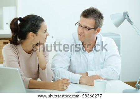 Happy young casual couple sitting  at desk working together at home office, smiling.