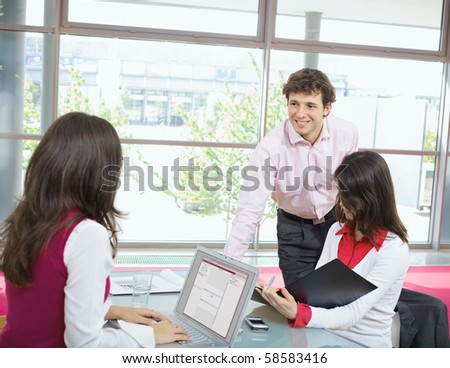 Young businesswomen working in office, using laptop computer, writing notes. Smiling businessman leaning on desk.