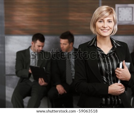 Happy young businesswoman standing in office hallway, holding personal organizer, smiling.?