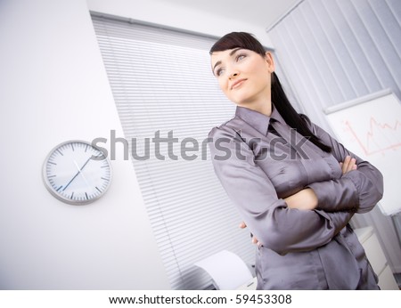 Portrait of young businesswoman standing with arms crossed in office, looking left. Low-angle shot.
