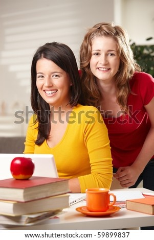 Teens learning at home with laptop computer and books looking at camera smiling.?
