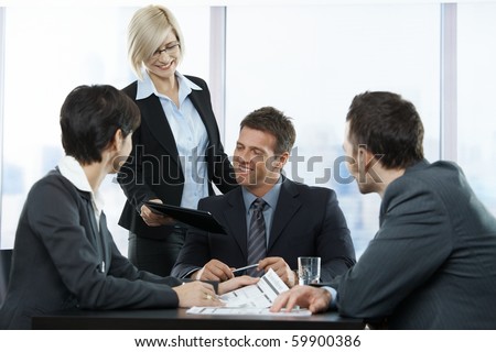 Happy businesspeople at meeting in office, standing assistant handing over contract to executive sitting with colleagues.?