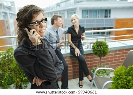 Business people talking on terrace outdoor of office building. Businesswoman in front using mobile phone.